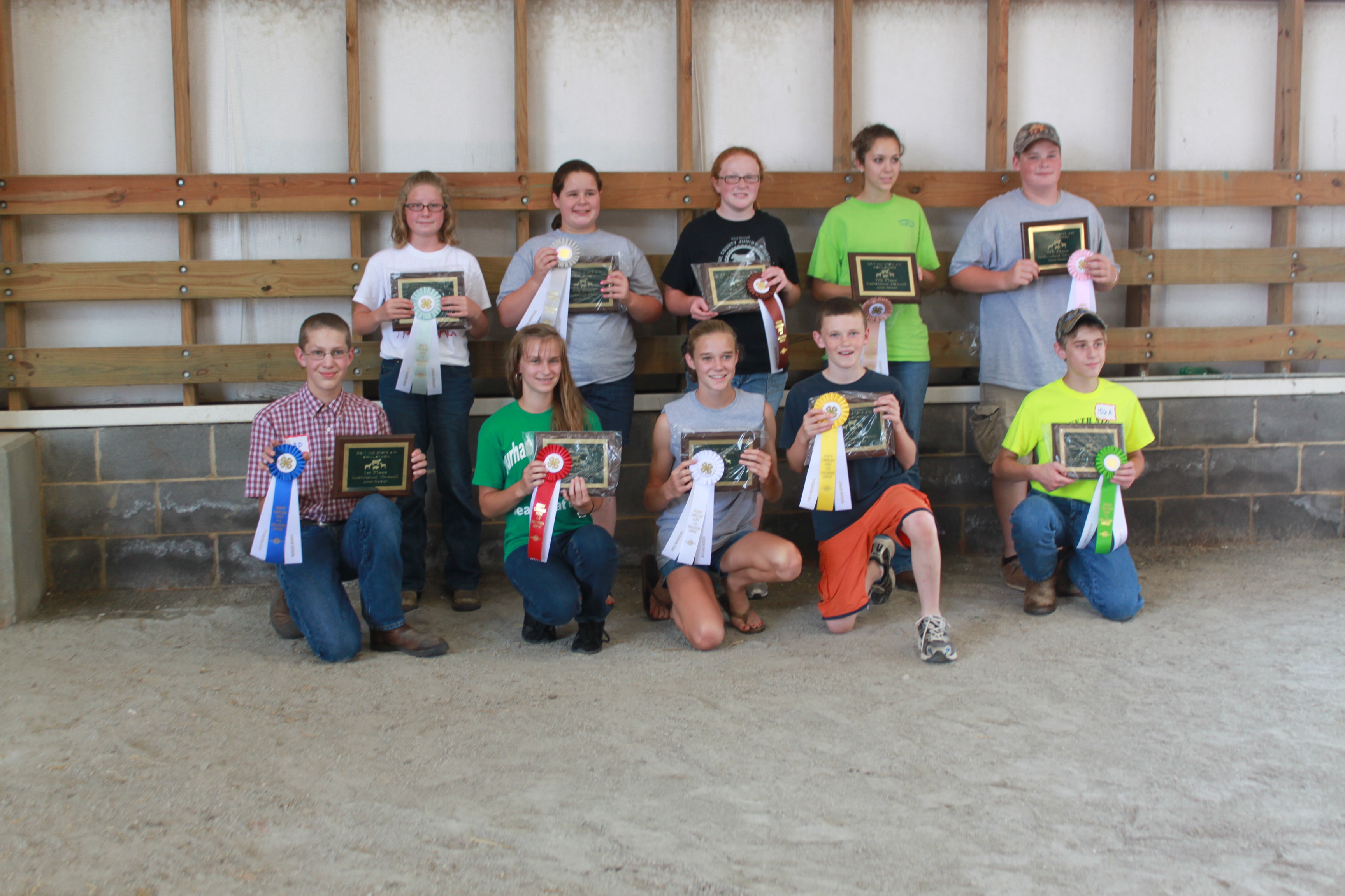 Children in a barn posing with appreciation plaques and ribbons.